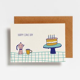 Colorful birthday cake with candles on a postcard, with a coffee mug and a sewing machine in the background.