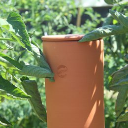  A tall, cylindrical orange compost bin for burying in the ground. The bin has several holes along the sides to allow for aeration and decomposition of organic matter.