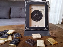 Astrology-themed chocolate gift set with a decorative picture frame and card. The set includes dark chocolate pieces with astrological symbols and designs.