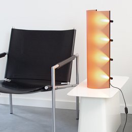  A tall, cylindrical lamp with a warm, amber-colored glow. The lamp has a modern, minimalist design and is mounted on the wall, providing ambient lighting.