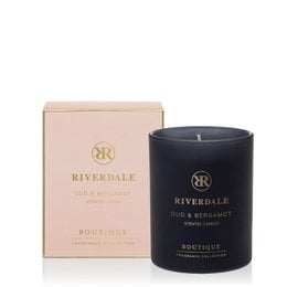  A tall, round, pink-colored scented candle in a black glass container, with the brand name "Riverdale" printed on the label.
