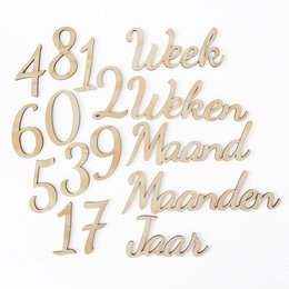 Wooden numbers and text spelling out "7 weeks" in Dutch, indicating a milestone or time period. The numbers and text are laid out on a beige background with a soft, textured fabric.