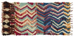A colorful, patterned area rug with a chevron design in shades of red, blue, and beige. The rug has a textured, shaggy appearance and tasseled edges.