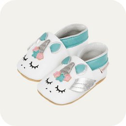  Soft leather baby booties with a unicorn design. Available in sizes 3-4 years, 2-3 years, 18-24 months, 12-18 months, 6-12 months, and 0-6 months. Features a white leather upper with a unicorn face, eyelashes, and floral accents in teal and pink.