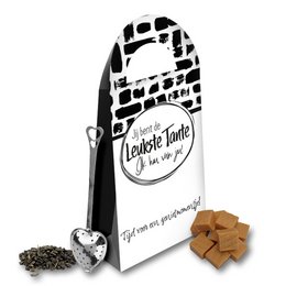A black and white package labeled "Favorite Auntie" containing tea leaves and tea bags, accompanied by a heart-shaped tea light and other cozy accessories.