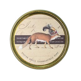  A round, scented candle with an image of a fox on the label. The candle is described as "Irresistibly Foxy" and is part of the "Tokyomilk" brand of scented candles.