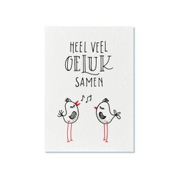 A greeting card with a playful, hand-drawn illustration of two stick figures celebrating together. The text on the card reads "Heel veel geluk samen" which translates to "Lots of luck together" in Dutch.