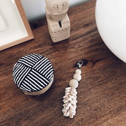 "White and black striped keychain with shell and tassel details."

The product appears to be a keychain with a round, striped pattern and a tassel made of white shells or beads. The keychain has a simple, minimalist design that would complement a variety of styles. This keychain could be used to accessorize bags, purses, or keys, and the neutral color palette would make it a versatile choice.