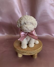 Plush cockapoo candle in natural, beige, brown, and gray colors. Soft, round shape with a pink ribbon.