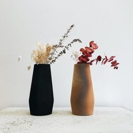 Two modern vases in black and tan colors, featuring a variety of dried flowers and foliage. The vases have a minimalist, geometric design with textured surfaces.