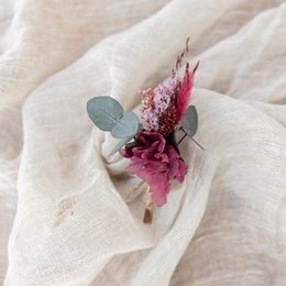 A pink floral brooch with dried flowers and greenery, suitable for formal occasions or as a wedding accessory.
