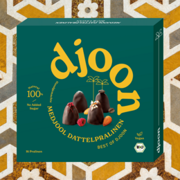 Organic date pralines in a mixed pack. The pralines are made with dates, roasted almonds, and other natural ingredients. The product has a variety of shapes and colors, including round and irregular forms.