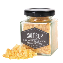 Yellow lemon-flavored salt flakes in a glass jar. The salt flakes have a bright, citrusy aroma and a crunchy texture.