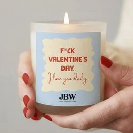 White cylindrical scented candle with "F*ck Valentine's Day" text, humorous anti-Valentine's design, cream colored wax.