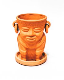Orange ceramic planter pot with a smiling face design, holding a green leafy plant.
