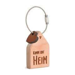Wooden keychain in the shape of a house with the text "Kom oit heim" (Come home in Norwegian). The keychain has a metal ring and a leather tag.