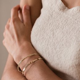 A gold-colored bangle bracelet with a minimalist, circular design and three small decorative elements.