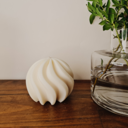 Soy wax candle with a swirled, round shape in an off-white color, displayed on a wooden surface.