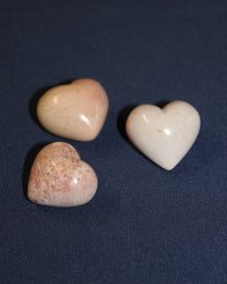 Three heart-shaped soapstone statues in various shades of beige and pink.