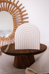  A decorative white object with a curved, arched shape, sitting on a wooden stand. The object appears to be made of a smooth, textured material, possibly ceramic or plaster. The design features a series of parallel lines or ridges that create a visually interesting and modern aesthetic.
