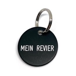 Black round keychain with the text "MEIN REVIER" printed in white. Metal ring for attaching to keys or other items.