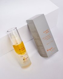 A bi-phase serum in a clear glass bottle with a yellow liquid inside. The bottle is packaged in a gray cardboard box with text and graphics.