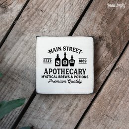 A square canvas print featuring the "Main Street Apothecary No1" logo in a vintage style. The print is available in multiple sizes, including 10x10, 15x15, and 20x20 inches. The image showcases the print against a rustic wooden background, along with other decorative elements like a glass jar and a pumpkin.
