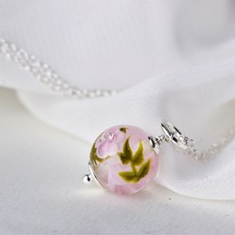 Delicate necklace with magnolia glass flower charm in pink and green hues. Elegant and nature-inspired pendant on a silver chain.