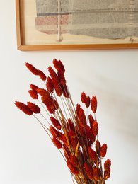 Dried orange phalaris flowers in a vase, with a decorative wooden sculpture on a wooden table.