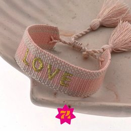  A woven bracelet in pink and gold colors, featuring the word "LOVE" in green text. The bracelet has a braided design with tassels at the ends.