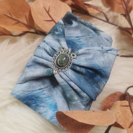 A blue and white tie-dye patterned headband with a silver-colored metal accent in the center.
The product is a headband with a tie-dye pattern in shades of blue and white. The headband has a silver-colored metal accent or embellishment in the center. The headband appears to be made of a soft, stretchy material and is suitable for small to standard head sizes.