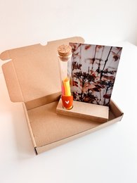 Rectangular gift box with tropical sunset print, containing a glass bottle with a cork stopper.