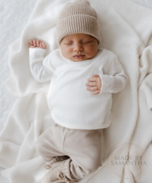 Soft, cozy merino wool baby bonnet in a neutral sand color. Features a warm, knitted design with ties to secure a snug fit.