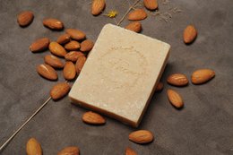 A rectangular bar of natural soap surrounded by whole almonds on a dark surface.