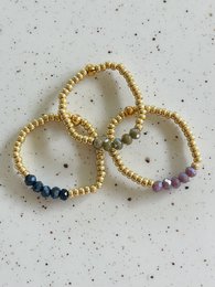 Assorted stacking rings with faceted beads in various colors, including gold, blue, and pink. The rings have a sparkly, textured appearance.