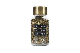 A glass tea infuser bottle with a gold-colored lid and a tea blend inside, featuring a variety of dried herbs and flowers.