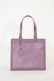 Lilac-colored square handbag with two handles and a circular metal accent.