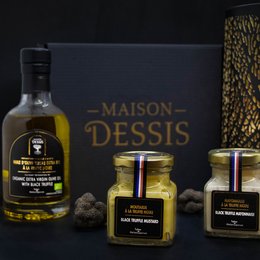 A gift box containing Maison Dessis truffles, including a bottle of truffle oil, a jar of truffle spread, and a jar of whole black truffles. The box is presented in a sleek black and gold design.