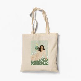 Organic tote bag featuring a whimsical illustration of a woman with long hair standing in a field of flowers. The bag is made of natural cotton and features sturdy handles for comfortable carrying.