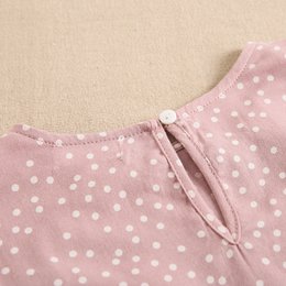  A long-sleeved, printed blouse for girls in a pink polka dot pattern. The blouse features a round neckline and ruched detailing on the sleeves.