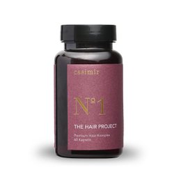 The Hair Project | Hair Complex is a supplement that promotes healthy hair growth. The product features a dark red bottle with a black cap. The supplement contains ingredients that may help strengthen and nourish hair.