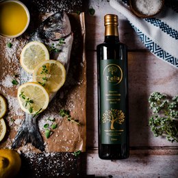 Premium extra virgin olive oil in a glass bottle with a green label. Surrounded by lemon slices, herbs, and other olive oil ingredients.