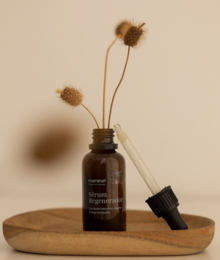 Regenerating serum in a glass bottle with a dropper, surrounded by yellow roses. The serum is a skincare product designed to rejuvenate and revitalize the skin.