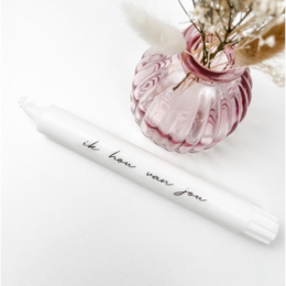  A tall, round, white candle in a pink glass vase with dried flowers. The candle has the text "Ik hou van jou" printed on it.