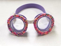 Colorful, donut-shaped swim goggles with a playful, fun design for kids. Features a pink frame with multicolored sprinkle-like accents.