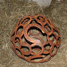 Rusty, round, patina-covered garden decoration made of horseshoe-shaped metal pieces, approximately 40 cm in diameter.