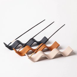 Curly incense holder in white birch, ebony black, and cedar/terracotta finishes. Wavy, sculptural design with metal accents.