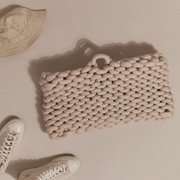 Oversized tote bag in nut brown, grey, black, ecru, and dusty pink colors. Made of a textured, woven material with a unique, chunky knit pattern.