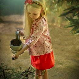 A pink and white floral print blouse with long sleeves and a ruffled collar. The blouse appears to be made of a lightweight, soft fabric and is suitable for a young girl.