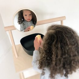 A round, wooden mirror for children's washbasin in a Montessori-inspired design. The mirror is mounted on a wooden frame, allowing children to easily see themselves while washing their hands.